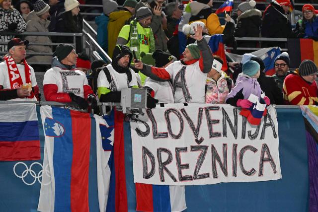 Solvenian fans react with flags of Slovenia during the ski jumping mixed team final round of the Milano Cortina 2026 Winter Olympic Games at Predazzo Ski Jumping Stadium in Predazzo (Val di Fiemme), on February 10, 2026. (Photo by Javier SORIANO / AFP)