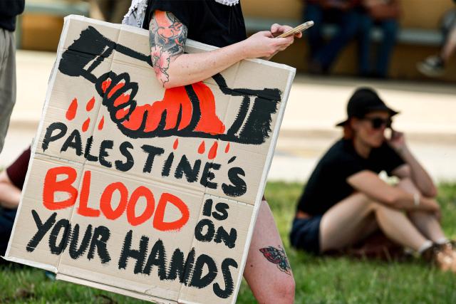A protester with a sign join others outside the Parliamment House building ahead of the meeting between Australia's Prime Minister Anthony Albanese and Israel's President Isaac Herzog in Canberra on February 11, 2026. Herzog's tightly secured, four-day trip aims to console Australia's Jewish community after the December shooting at Sydney's Bondi Beach that killed 15 people at a Hanukkah festival. (Photo by DAVID GRAY / AFP)