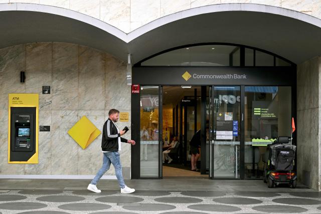 A man walks past a branch of the Commonwealth Bank of Australia (CBA) in Melbourne on February 11, 2026, after the bank posted a cash net profit after tax of 5.4 billion Australian dollars (3.85 billion US) for the first half of the 2025-26 financial year, up 6% compared to the same period last year. (Photo by William WEST / AFP)