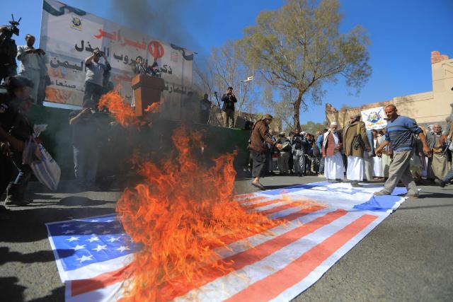 TOPSHOT - Protesters set fire on a makeshift US and Israeli flag during a demonstration outside the former US embassy building in the Huthi-controlled capital Sanaa on February 11, 2026, marking the anniversary of the US withdrawal from the country in 2015. (Photo by Ahmed Mohammed / AFP)