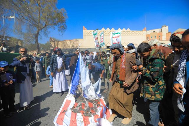 Protesters step on a makeshift US and Israeli flag during a demonstration outside the former US embassy building in the Huthi-controlled capital Sanaa on February 11, 2026, marking the anniversary of the US withdrawal from the country in 2015. (Photo by Ahmed Mohammed / AFP)