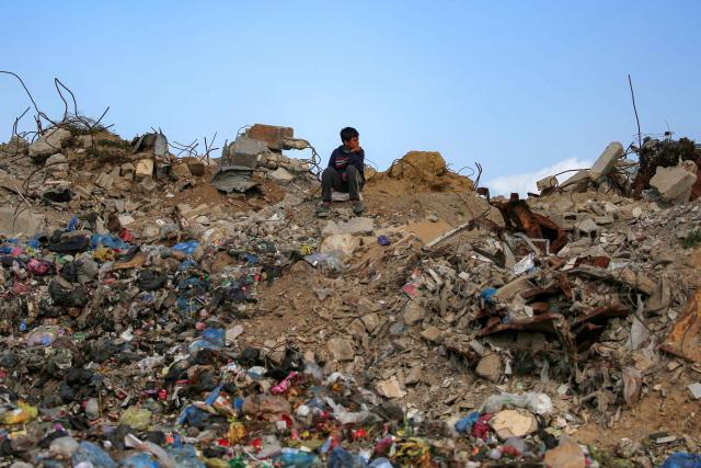 A boy sits on a mound of rubble and waste at the Maghazi camp for Palestinian refugees in the central Gaza Strip on February 11, 2026. Since October 10, a fragile US-sponsored truce in Gaza has largely halted the fighting between Israeli forces and Hamas, but both sides have alleged frequent violations. (Photo by Eyad BABA / AFP)