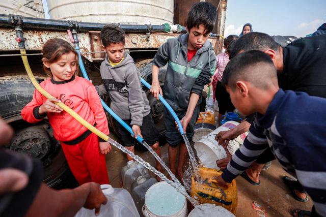 Children use hoses to fill up water containers from a mobile cistern in the Maghazi camp for Palestinian refugees in the central Gaza Strip on February 11, 2026. Since October 10, a fragile US-sponsored truce in Gaza has largely halted the fighting between Israeli forces and Hamas, but both sides have alleged frequent violations. (Photo by Eyad BABA / AFP)