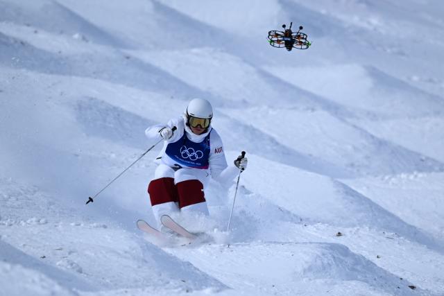 A drone follows Austria's Katharina Ramsauer as she competes in the freestyle skiing women's moguls qualification 2 during the Milano Cortina 2026 Winter Olympic Games at Livigno Aerials & Moguls Park, in Livigno (Valtellina), on February 11, 2026. (Photo by Kirill KUDRYAVTSEV / AFP)