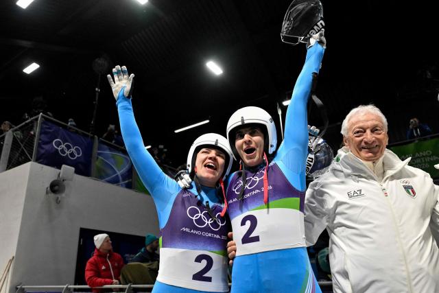 Italy's Andrea Voetter and Italy's Marion Oberhofer celebrate with Italy's Olympic Committee (CONI) president Luciano Buonfiglio (R) after crossing the finish line to win the luge women's doubles run 2 at Cortina Sliding Centre during the Milano Cortina 2026 Winter Olympic Games in Cortina d'Ampezzo on February 11, 2026. (Photo by Tiziana FABI / AFP)