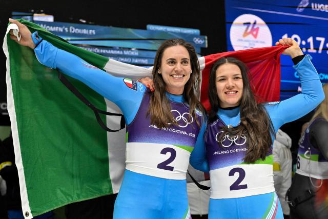 Italy's Andrea Voetter (L) and Italy's Marion Oberhofer (R) celebrate after crossing the finish line to win the luge women's doubles at Cortina Sliding Centre during the Milano Cortina 2026 Winter Olympic Games in Cortina d'Ampezzo on February 11, 2026. (Photo by Tiziana FABI / AFP)