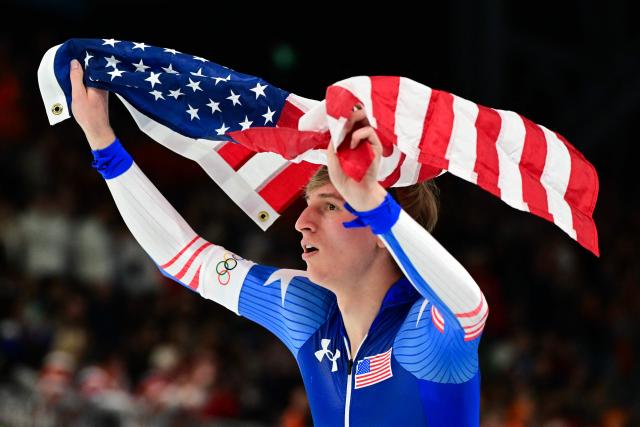USA's Jordan Stolz carries a flag after competing to win the gold medal in the speed skating men's 1000m event during the Milano Cortina 2026 Winter Olympic Games at Milano Speed Skating Stadium in Milan on February 11, 2026. (Photo by Piero CRUCIATTI / AFP)