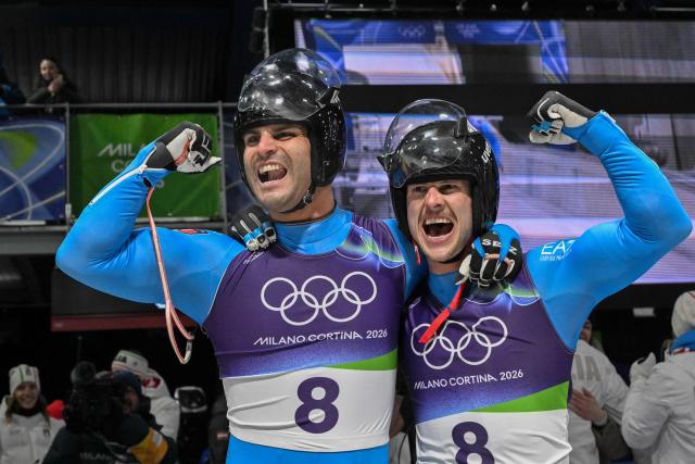 Italy's Emanuel Rieder (L) and Simon Kainzwaldner celebrate winning the gold medal in the finish area of the luge men's doubles at Cortina Sliding Centre during the Milano Cortina 2026 Winter Olympic Games in Cortina d'Ampezzo on February 11, 2026. (Photo by Tiziana FABI / AFP)