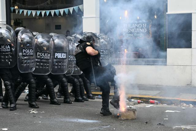 A policeman kicks a box with gunpowder during a protest of trade unionists against the labor reform debate taking place in the National Congress in Buenos Aires on February 11, 2026. Argentine police fired tear gas and used water cannon on February 11 to disperse demonstrators, who threw rocks and firebombs outside Congress during a Senate debate over radical labor reforms. (Photo by Luis ROBAYO / AFP)