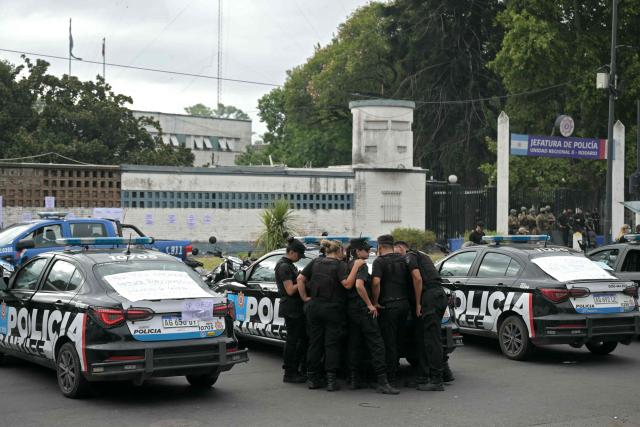 Santa Fe provincial police officers watch the speech of Governor Maximiliano Pullaro on a cell phone during a protest in front of the force's headquarters demanding higher salaries and improved mental health support amid growing pressure from long working hours, in Rosario, Santa Fe Province, Argentina, on February 11, 2026. Dozens of police officers staged a rebellion demanding higher salaries and improved mental health care in the Argentine city of Rosario, in protests that continued until the early hours of February 11 and were set to resume during the day, according to the demonstrators, who expressed dissatisfaction with the local government's response. (Photo by Juan Mabromata / AFP)