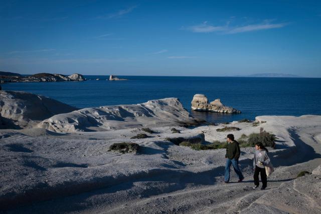This picture taken on February 3, 2026, shows people walking at Sarakiniko Beach in the Greek Aegean island of Milos. On the sloping coastline facing the Aegean Sea, the vast construction site looks like a gaping wound inflicted on the volcanic rock. ‘An ecological crime’ according to Manolis Mikelis, mayor of Milos, the Greek island in the Cyclades where this luxury hotel has begun extensive expansion work. "The geological uniqueness of Milos is known throughout the world. We don't want its identity to change," grumbles the mayor. Private villas and high-end complexes: the entire archipelago, known for its whitewashed houses and blue church domes, is caught up in a real estate fever fuelled by the tourism boom. (Photo by Aris MESSINIS / AFP)
