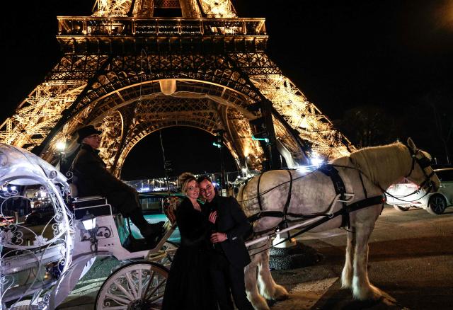 Dutch couple, Shirley Wijgaarts and Sander Castel, pose next to a fairytale horse drawn carriage in front of the Eiffel Tower during their marriage proposal, in central Paris, on February 07, 2026. In Paris, marriage proposals take on a cinematic flair, complete with Cinderella's carriage, private terraces, and bespoke scenarios, creating a lucrative market fueled by international clients. (Photo by STEPHANE DE SAKUTIN / AFP)