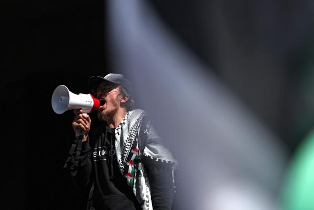 A protester speaks through megaphones next to a Palestinian flag in front of police officers as they cordon off a venue during the visit of Israel’s President Isaac Herzog in Melbourne on February 12, 2026. Herzog's tightly secured, four-day trip aims to console Australia's Jewish community after the December shooting at Sydney's Bondi Beach that killed 15 people at a Hanukkah festival. (Photo by MARTIN KEEP / AFP)