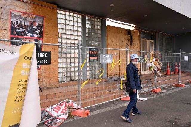 A man walks past banners and flowers hanging from a security fence outside the torched Adass Israel Synagogue in Melbourne on February 12, 2026. Israel’s President Isaac Herzog was scheduled to visit the synagogue during his visit to Melbourne, but the event was cancelled. Herzog's tightly secured, four-day trip aims to console Australia's Jewish community after the December shooting at Sydney's Bondi Beach that killed 15 people at a Hanukkah festival. (Photo by WILLIAM WEST / AFP)