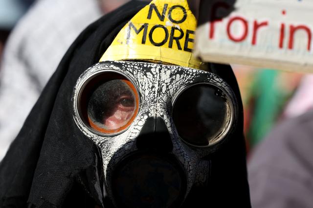 A protester wears a gas mask as he holds a placard outside Flinders Street station during the visit of Israel’s President Isaac Herzog in Melbourne on February 12, 2026. Herzog's tightly secured, four-day trip aims to console Australia's Jewish community after the December shooting at Sydney's Bondi Beach that killed 15 people at a Hanukkah festival. (Photo by MARTIN KEEP / AFP)
