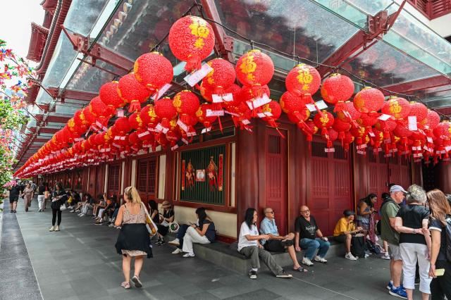 People rest outside the Buddha Tooth Relic Temple, which is decorated with lanterns in preparation for the upcoming Lunar New Year, in the Chinatown district of Singapore on February 12, 2026. (Photo by Roslan RAHMAN / AFP)