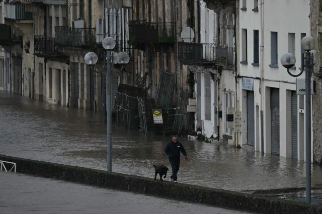 TOPSHOT - A pedestrian walks his dog along a submerged street as floodwaters from the swollen Garonne river inundate streets in La Reole, south-western France, on February 12, 2026, during the storm Nils triggering flooding across the area. Vigicrues, France's flood monitoring service, warned of very significant overflows along the Garonne river with water levels in the La RÈole sector comparable to the major floods of February 2021. (Photo by PHILIPPE LOPEZ / AFP)