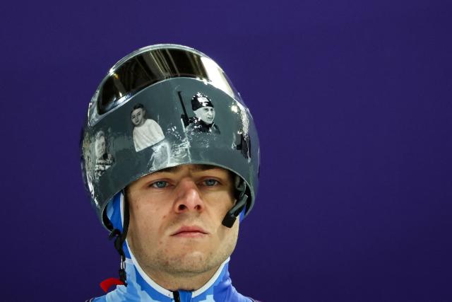 In this file photo taken on February 9, 2026 Ukraine's Vladyslav Heraskevych wears a helmet with pictures of Ukrainian sportsmen and women, victims of his country's war with Russia, prior to taking part in the skeleton men's training session at Cortina Sliding Centre during the Milano Cortina 2026 Winter Olympic Games in Cortina d'Ampezzo. Ukrainian skeleton racer Vladyslav Heraskevych was disqualified from the Winter Olympics on February 12, 2026 after refusing to back down over his banned helmet, which depicts victims of his country's war with Russia. In a statement, the International Olympic Committee said Heraskevych is "not allowed to participate at Milano-Cortina 2026 after refusing to adhere to the IOC athlete expression guidelines". (Photo by FRANCK FIFE / AFP)