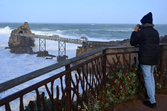 A man takes photograph of waves crashing at the Rock of the Virgin (Rocher de la Vierge) in Biarritz, southwestern France on February 12, 2026, as storm Nils hits the area. Accompanied by winds exceeding 160 km/h, Storm Nils swept across several regions of France on February 12, 2026, causing the death of a lorry driver in the Landes and damage, leaving 850,000 homes without electricity, particularly in the southwest. (Photo by Gaizka IROZ / AFP)