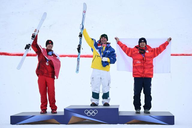 (From L) Silver medallist Canada's Mikael Kingsbury, gold medallist Australia's Cooper Woods and bronze medallist Japan's Ikuma Horishima celebrate on the podium after the freestyle skiing men's moguls final during the Milano Cortina 2026 Winter Olympic Games at Livigno Aerials & Moguls Park, in Livigno (Valtellina), on February 12, 2026. (Photo by Kirill KUDRYAVTSEV / AFP)