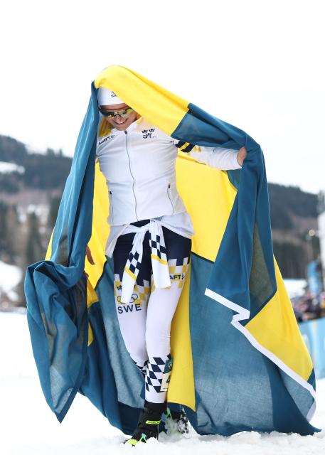 Sweden's Frida Karlsson starts to celebrate with Sweden's flag as the race is not over yet, during the women's cross-country skiing 10km interval start free event of the Milano Cortina 2026 Winter Olympic Games at Tesero Cross-Country Skiing Stadium in Lago di Tesero (Val di Fiemme), on February 12, 2026. (Photo by Anne-Christine POUJOULAT / AFP)