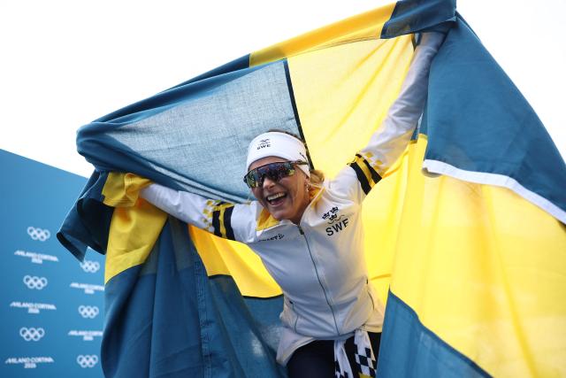 Gold medallist Sweden's Frida Karlsson celebrates with Sweden's flag during the women's cross-country skiing 10km interval start free event of the Milano Cortina 2026 Winter Olympic Games at Tesero Cross-Country Skiing Stadium in Lago di Tesero (Val di Fiemme), on February 12, 2026. (Photo by Anne-Christine POUJOULAT / AFP)