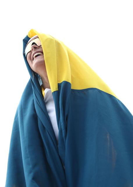 Sweden's Frida Karlsson starts to celebrate with Sweden's flag as the race is not over yet, during the women's cross-country skiing 10km interval start free event of the Milano Cortina 2026 Winter Olympic Games at Tesero Cross-Country Skiing Stadium in Lago di Tesero (Val di Fiemme), on February 12, 2026. (Photo by Anne-Christine POUJOULAT / AFP)