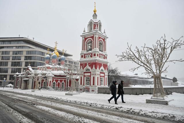 People walk at the Zaryadye park on a snowy day in central Moscow on February 12, 2026. (Photo by Hector RETAMAL / AFP)
