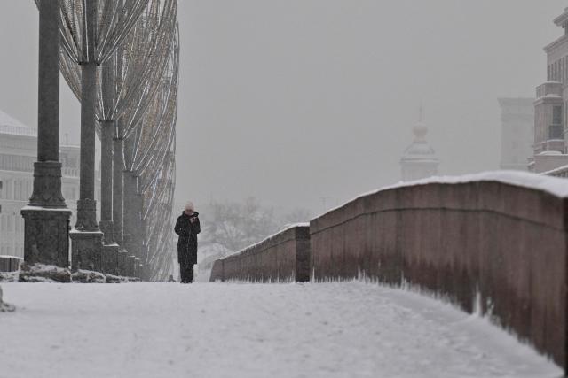 A woman walks along a bridge over the Moskva river on a snowy day in central Moscow on February 12, 2026. (Photo by Hector RETAMAL / AFP)