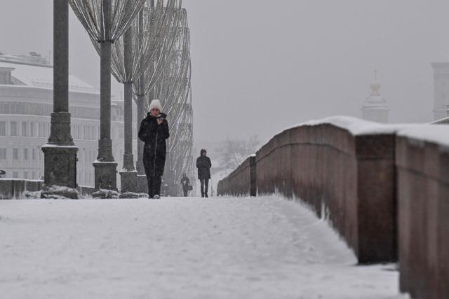 People walk along a bridge over the Moskva river on a snowy day in central Moscow on February 12, 2026. (Photo by Hector RETAMAL / AFP)