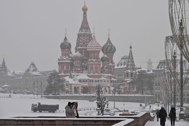 A woman uses a smartphone on a bridge over the Moskva river, with St. Basil's cathedral seen in distance, during a snowy day in central Moscow on February 12, 2026. (Photo by Hector RETAMAL / AFP)