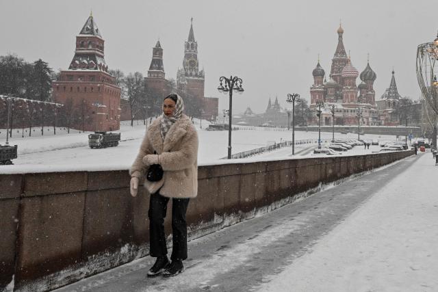 A woman walks along a bridge over the Moskva river, with the Kremlin's Spasskaya tower and St. Basil's cathedral seen in distance, during a snowy day in central Moscow on February 12, 2026. (Photo by Hector RETAMAL / AFP)