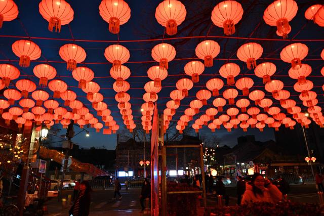 People walk past lantern decorations at Yaojiang Hutong, an alley of traditional houses in Beijing on February 12, 2026, on the eve of the Lunar New Year of the Horse. (Photo by ADEK BERRY / AFP)