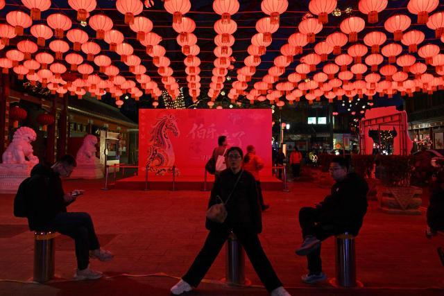 People sit under lantern decorations at Yaojiang Hutong, an alley of traditional houses in Beijing on February 12, 2026, on the eve of the Lunar New Year of the Horse. (Photo by ADEK BERRY / AFP)