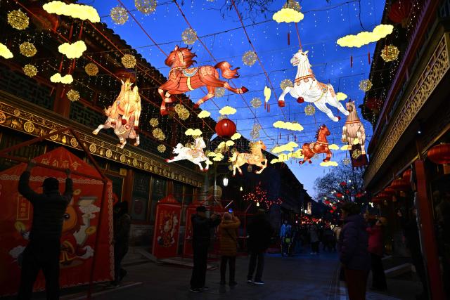 People walk past lantern decorations at Yaojiang Hutong, an alley of traditional houses in Beijing on February 12, 2026, on the eve of the Lunar New Year of the Horse. (Photo by ADEK BERRY / AFP)