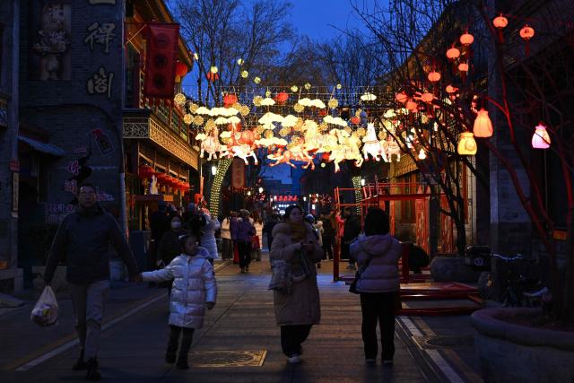 People walk past lantern decorations at Yaojiang Hutong, an alley of traditional houses in Beijing on February 12, 2026, on the eve of the Lunar New Year of the Horse. (Photo by ADEK BERRY / AFP)