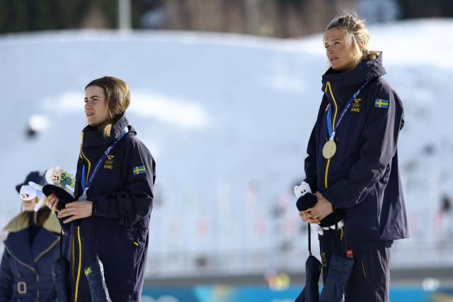 Silver medallist Sweden's Ebba Andersson (L) and gold medallist Sweden's Frida Karlsson  listen to the national anthems on the podium for the women's cross-country skiing 10km interval start free event of the Milano Cortina 2026 Winter Olympic Games at Tesero Cross-Country Skiing Stadium in Lago di Tesero (Val di Fiemme), on February 12, 2026. (Photo by Anne-Christine POUJOULAT / AFP)