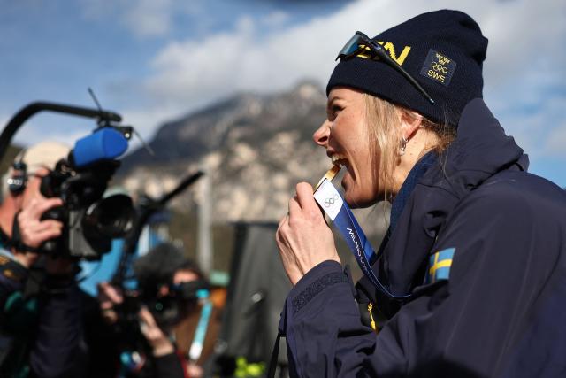 Gold medallist Sweden's Frida Karlsson bites her medal as she celebrates after the podium ceremony for the women's cross-country skiing 10km interval start free event of the Milano Cortina 2026 Winter Olympic Games at Tesero Cross-Country Skiing Stadium in Lago di Tesero (Val di Fiemme), on February 12, 2026. (Photo by Anne-Christine POUJOULAT / AFP)