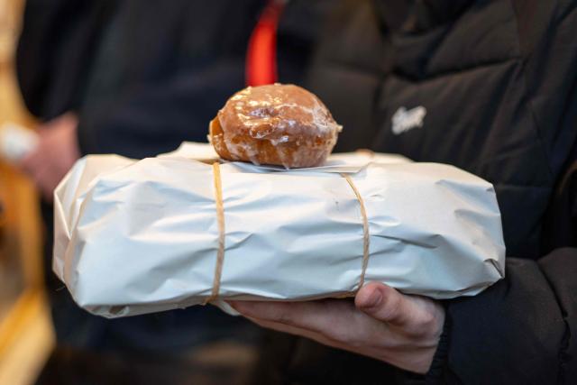A customer holds a package of traditional, marmalade-filled "paczki" - doughnuts, which he just bought after spending over 4 hours queuing in front of one of the most popular and believed to be the oldest "paczki" bakeries in Warsaw to celebrate the end of carnival on February 12, 2026. (Photo by Wojtek RADWANSKI / AFP)