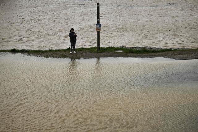 A woman stands on a path surrounded by flood in Marmande, south-western France, on February 12, 2026, as storm Nils triggers exceptional flooding along the Garonne river with authorities maintaining red alert status across the Gironde department. Accompanied by winds exceeding 160 km/h, Storm Nils swept across several regions of France on Thursday, causing the death of a lorry driver in the Landes and damage, leaving 850,000 homes without electricity, particularly in the southwest. (Photo by Philippe LOPEZ / AFP)