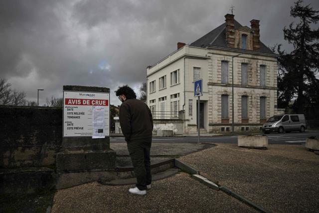 A man reads a flood warning sign on the banks of the Garonne river in Marmande, south-western France, on February 12, 2026, as storm Nils triggers exceptional flooding along the Garonne river with authorities maintaining red alert status across the Gironde department. Accompanied by winds exceeding 160 km/h, Storm Nils swept across several regions of France on Thursday, causing the death of a lorry driver in the Landes and damage, leaving 850,000 homes without electricity, particularly in the southwest. (Photo by Philippe LOPEZ / AFP)