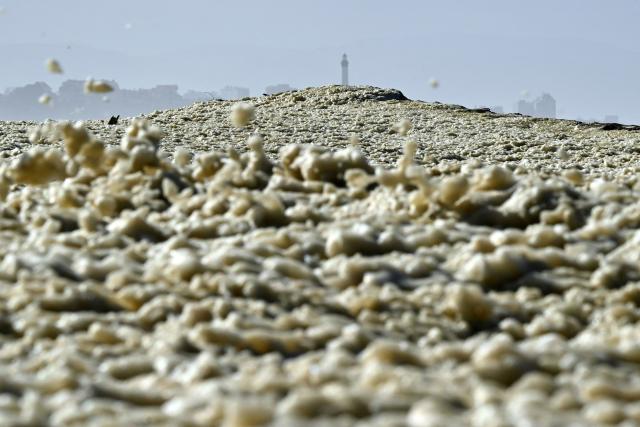 This photograph shows sea foam on La Barre beach with the Biarritz lighthouse in the background in Anglet, as the storm named Nils hits southwestern France coastline on February 12, 2026. (Photo by Gaizka IROZ / AFP)