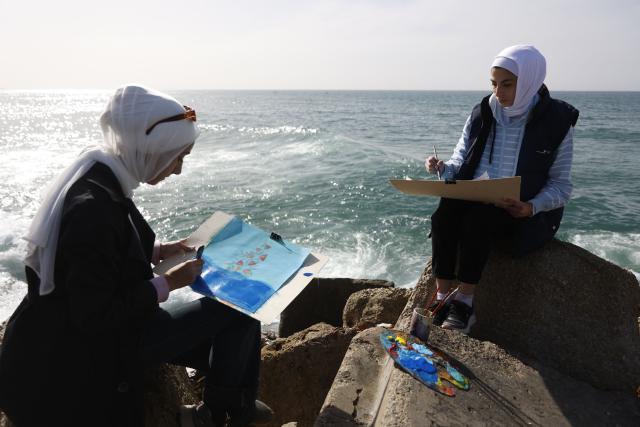 Young women paint at the Gaza City seaport on February 12, 2026, as part of the Breath and Paint workshop for girls in Gaza, aiming to provide a safe space for venting emotions and dealing with the effects of trauma through art and painting. (Photo by Omar AL-QATTAA / AFP)