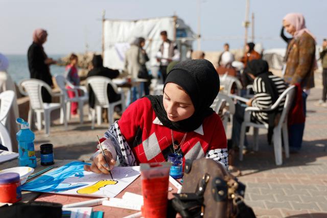 Young women paint at the Gaza City seaport on February 12, 2026, as part of the Breath and Paint workshop for girls in Gaza, aiming to provide a safe space for venting emotions and dealing with the effects of trauma through art and painting. (Photo by Omar AL-QATTAA / AFP)