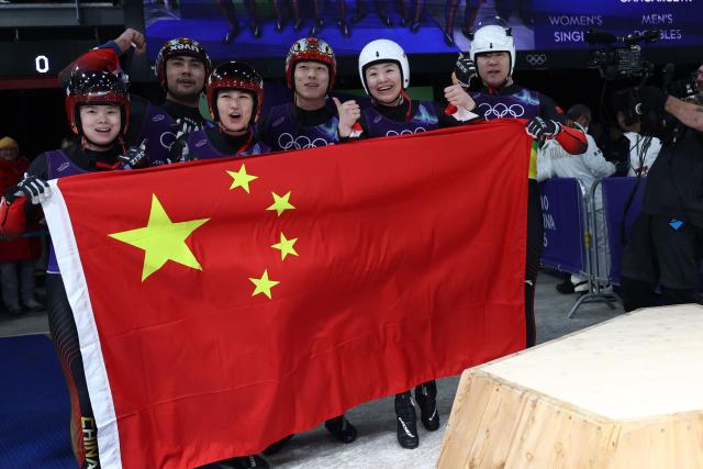 China's Wang Peixuan, China's Hou Shuo, China's Jubayi Saikeyi, China's Bao Zhenyu, China's Gulijienaiti Adikeyoumu and China's Zhao Jiaying hold a Chinese flag after competing in the luge team mixed relay at Cortina Sliding Centre during the Milano Cortina 2026 Winter Olympic Games in Cortina d'Ampezzo on February 12, 2026. (Photo by Franck FIFE / AFP)