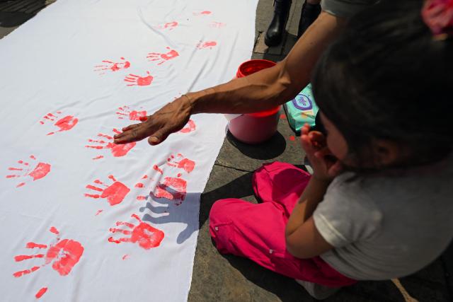 People stamp their painted hands on a cloth during a demonstration to commemorate the International Day Against the Use of Child Soldiers, also known as Red Hand Day, at Bolivar Square in Bogota on February 12, 2026. (Photo by Luis ACOSTA / AFP)