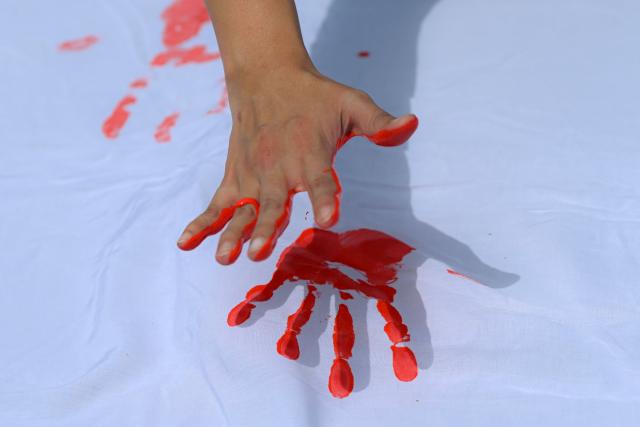 A person stamps his painted hand on a cloth during a demonstration to commemorate the International Day Against the Use of Child Soldiers, also known as Red Hand Day, at Bolivar Square in Bogota on February 12, 2026. (Photo by Luis ACOSTA / AFP)