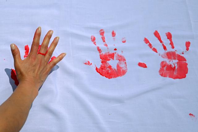 A woman stamps her painted hand on a cloth during a demonstration to commemorate the International Day Against the Use of Child Soldiers, also known as Red Hand Day, at Bolivar Square in Bogota on February 12, 2026. (Photo by Luis ACOSTA / AFP)
