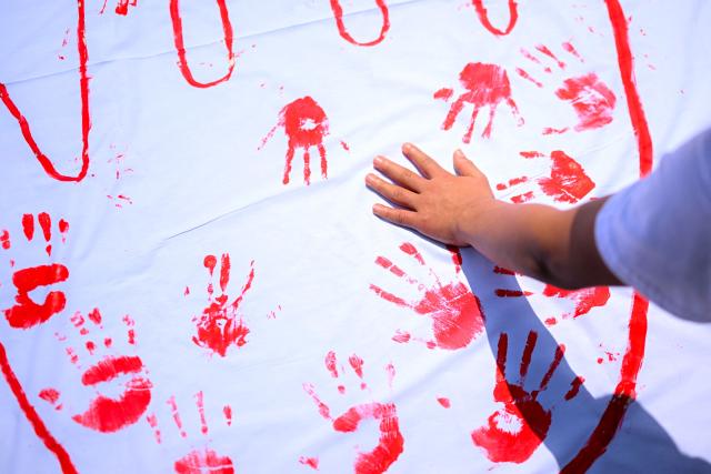 A woman stamps her painted hand on a cloth during a demonstration to commemorate the International Day Against the Use of Child Soldiers, also known as Red Hand Day, at Bolivar Square in Bogota on February 12, 2026. (Photo by Luis ACOSTA / AFP)