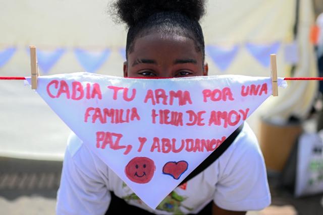 A girl poses behind a scarf reading "Trade your weapon for a family full of love, peace and abundance” during a demonstration to commemorate the International Day Against the Use of Child Soldiers, also known as Red Hand Day, at Bolivar Square in Bogota on February 12, 2026. (Photo by Luis ACOSTA / AFP)